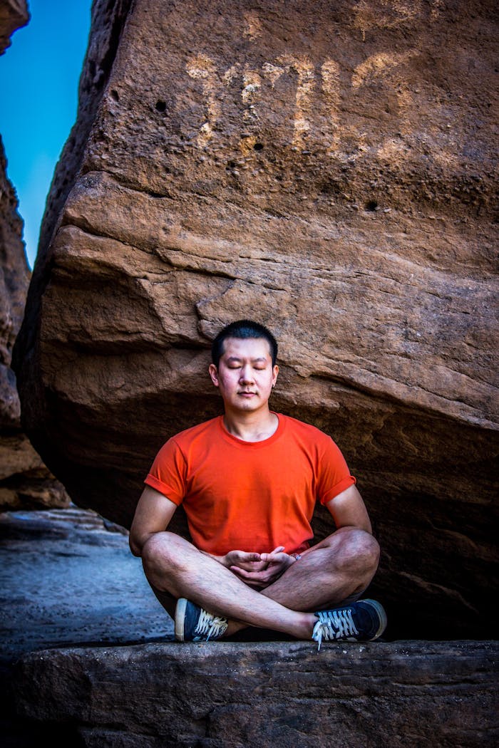 Man in meditation pose outdoors against a rocky backdrop, serene and focused.