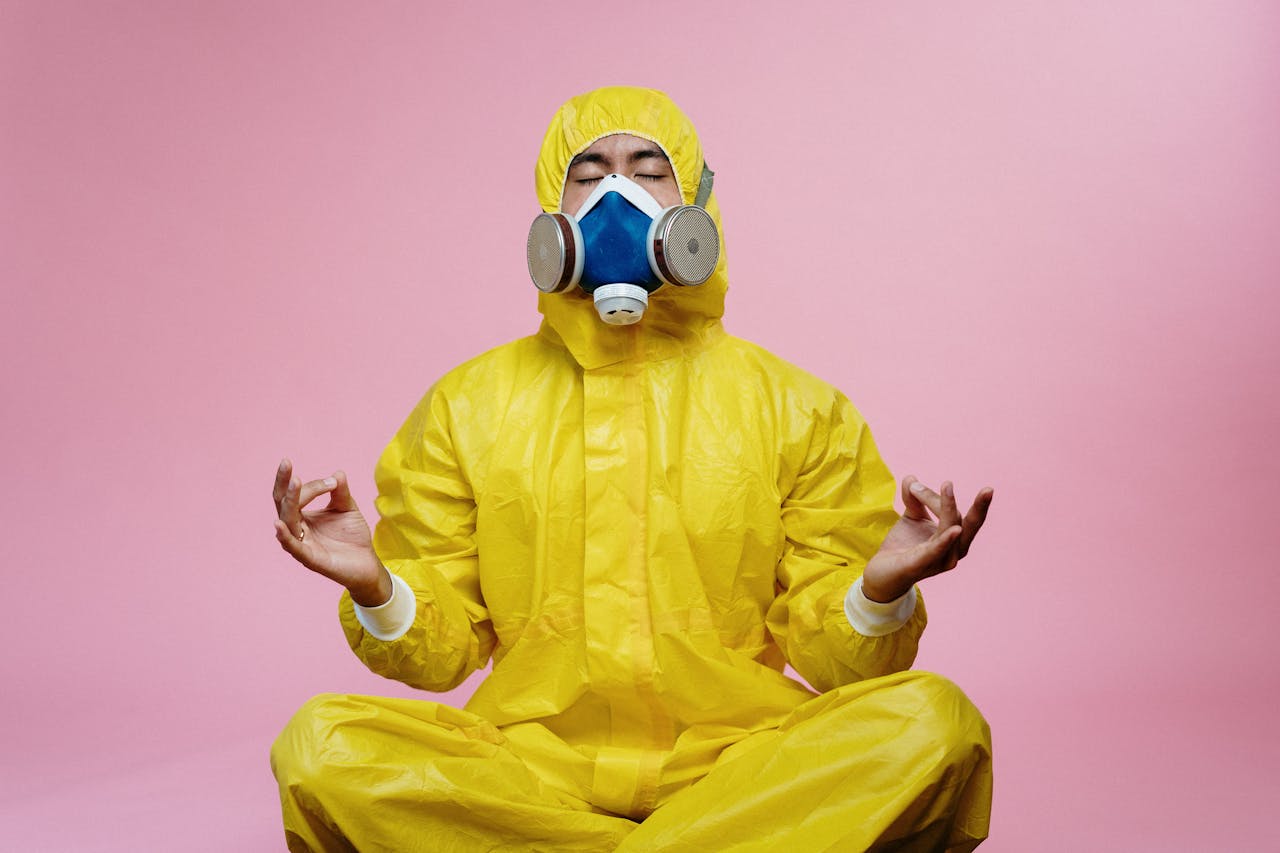 Man in protective suit and respirator practicing meditation against pink backdrop.